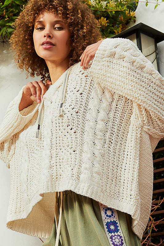 Cream medium-gauge knit sweater that shapes a v-neckline and long sleeves with drop shoulders. The boxy, roomy bodice falls to a slightly cropped hem and is topped with a hoodie. 